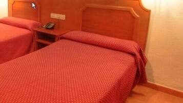 Een hotelkamer met twee bedden, elk met een rode sprei. Er is een nachtkastje met een telefoon en een lichtschakelaar aan de muur.