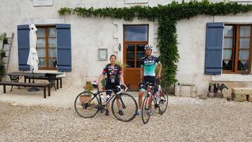 Two people on bicycles in front of a building with a gravel ground.