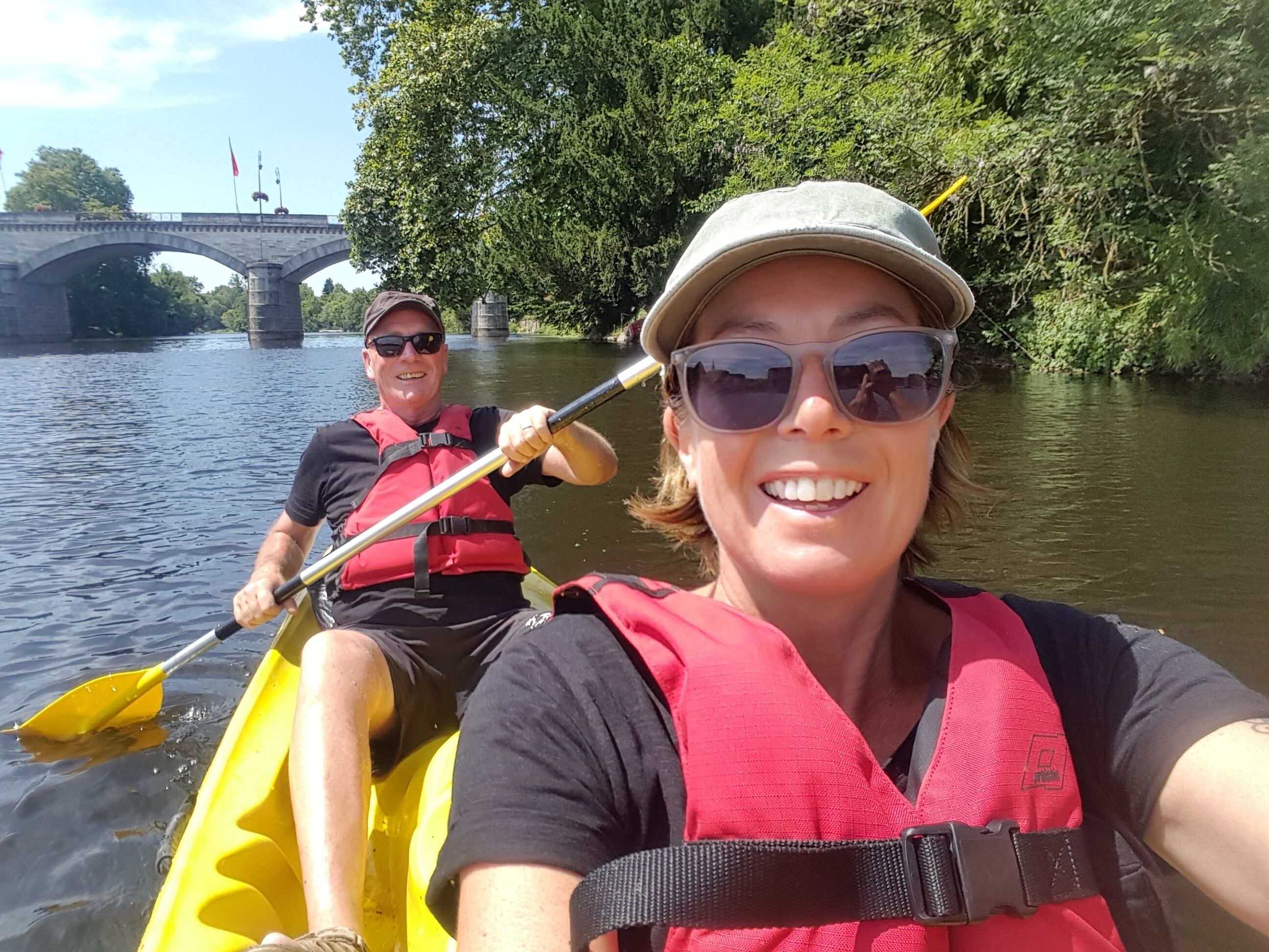 Deux personnes pratiquent le kayak sur une rivière, avec un pont en arrière-plan.