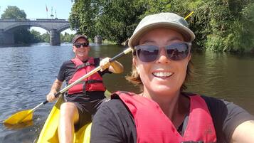 Deux personnes pratiquent le kayak sur une rivière, avec un pont en arrière-plan.