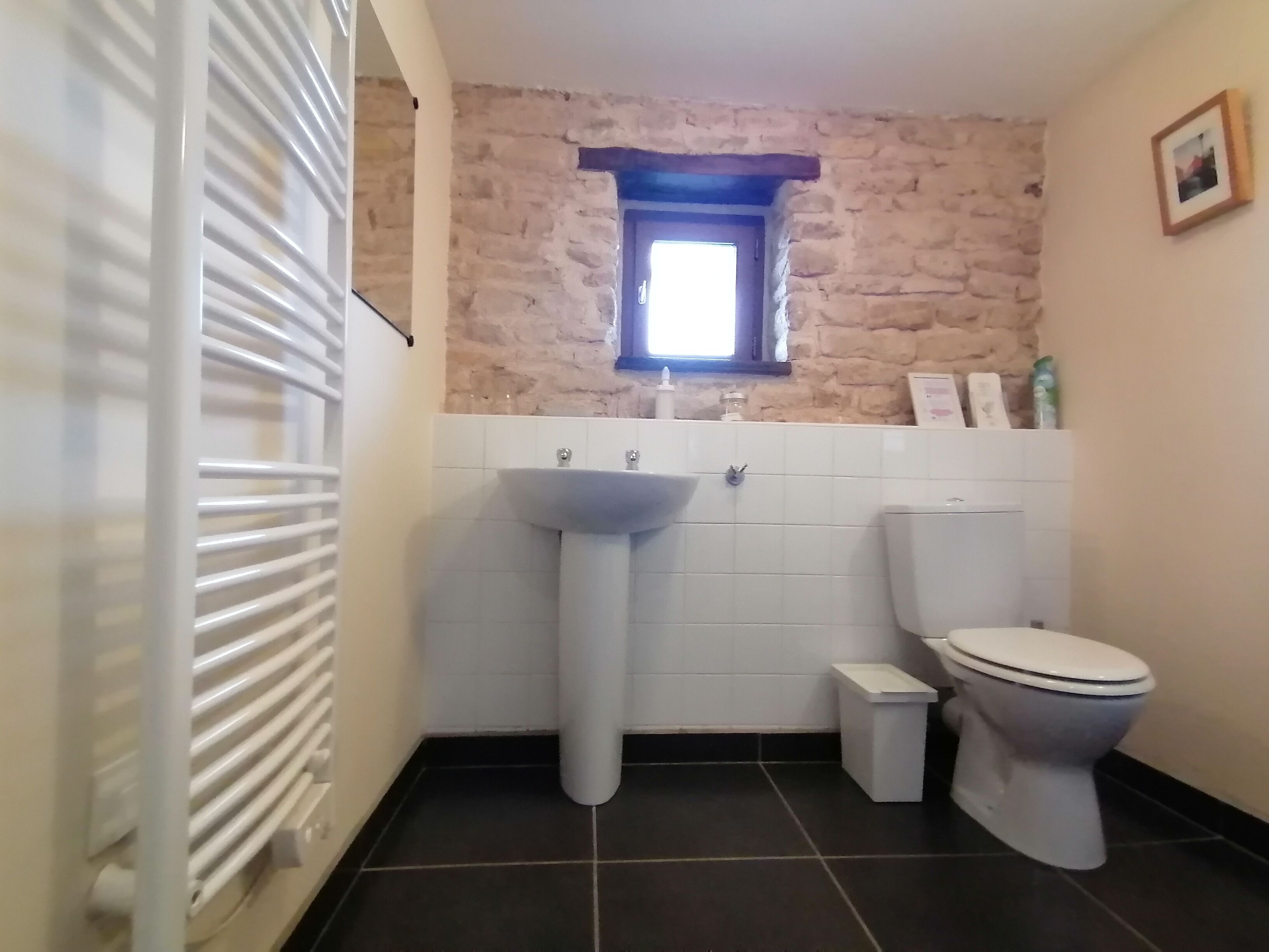 Un baño con un lavamanos blanco, un inodoro y una ventana sobre el lavamanos.