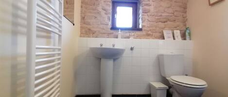Un baño con un lavamanos blanco, un inodoro y una ventana sobre el lavamanos.