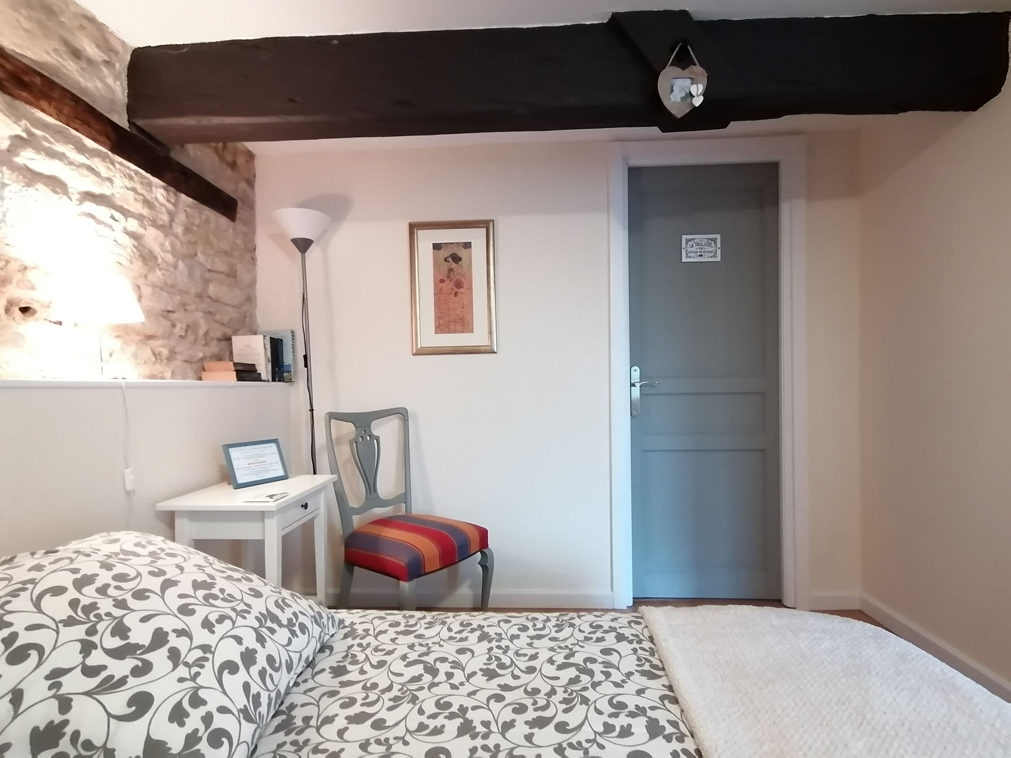 Un dormitorio con cama, escritorio, silla, lámpara y puerta.