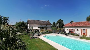 A swimming pool with lounge chairs, a grassy area, and two buildings with red-tiled roofs.