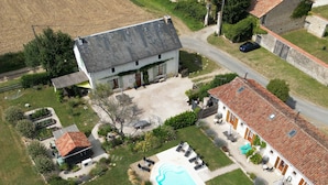 Vista aérea de una propiedad con piscina, jardín y una pequeña casa con techo de tejas.