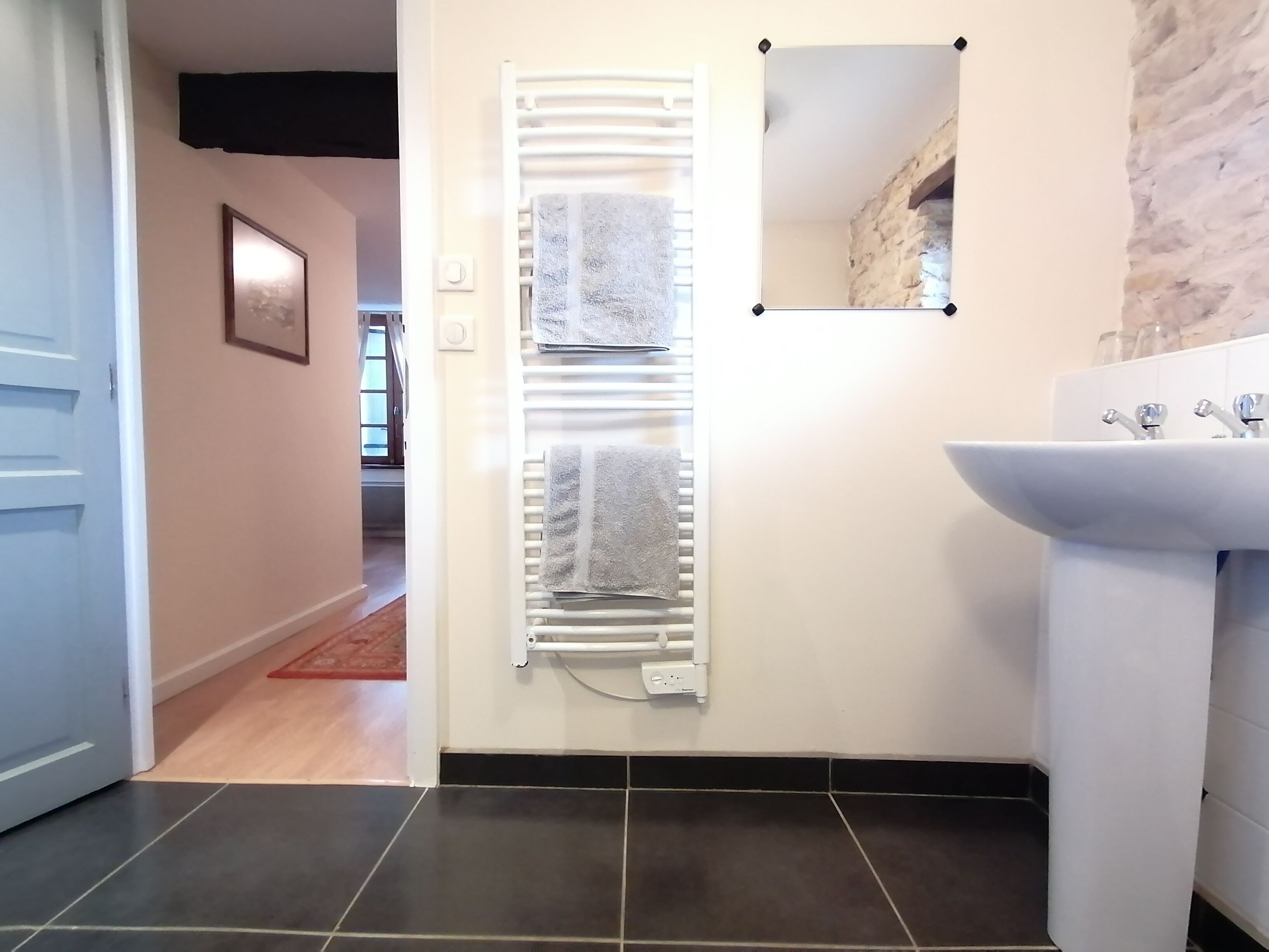 Une salle de bain moderne avec un lavabo blanc, un porte-serviettes avec deux serviettes et un miroir.