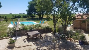 Patio con piscina, mesa de madera y sillas, rodeado de plantas en macetas y una valla de madera.