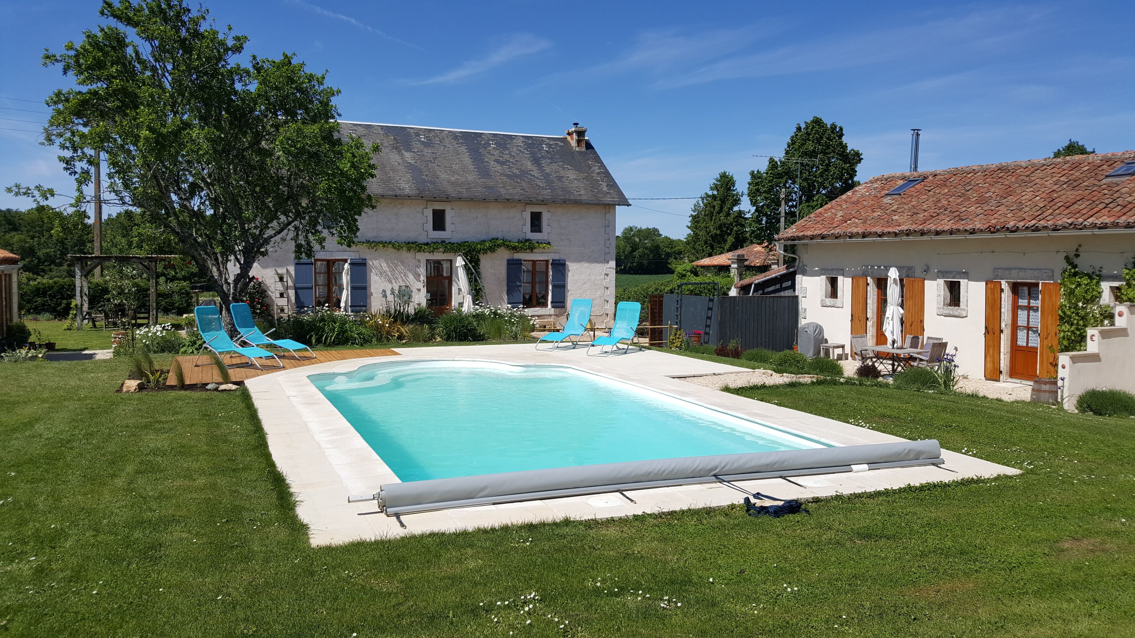 Una piscina con sillas azules, césped y una casa con tejado de baldosas.