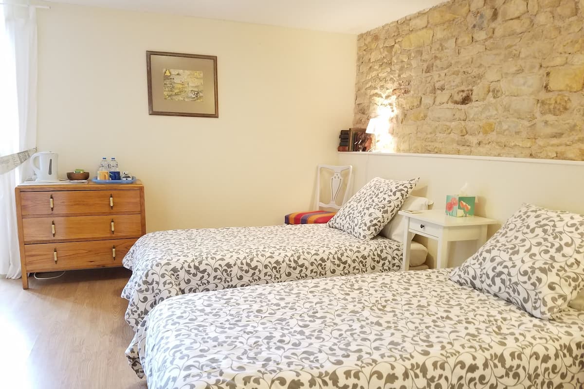 Un dormitorio con dos camas, un aparador, una mesita de noche, una pared de piedra y un cuadro enmarcado en la pared.