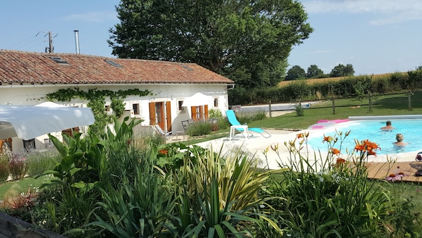Una villa con techo de tejas, piscina y jardín con diversas plantas.