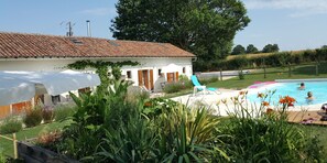 Una villa con techo de tejas, piscina y jardín con diversas plantas.