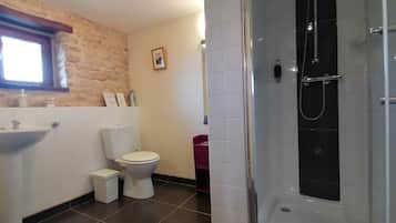 A bathroom with a stone wall, a white sink, a toilet, and a glass-enclosed shower.