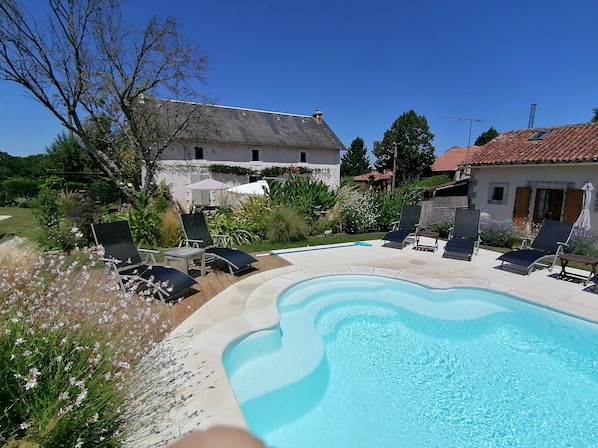 A swimming pool with lounge chairs, surrounded by a garden with various plants and a house in the background. - La Vieille Gorce (Asnois)