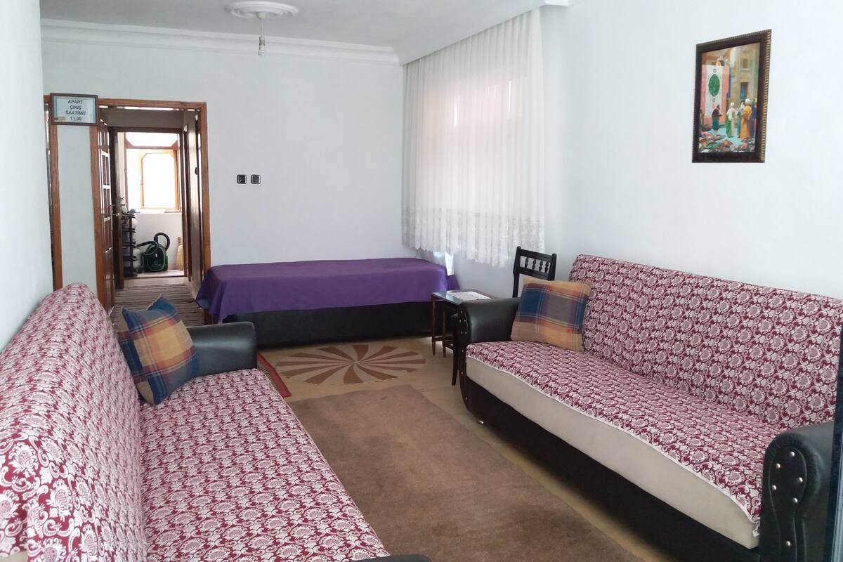 A room with a sofa set, a bed, a desk, and a window with curtains.