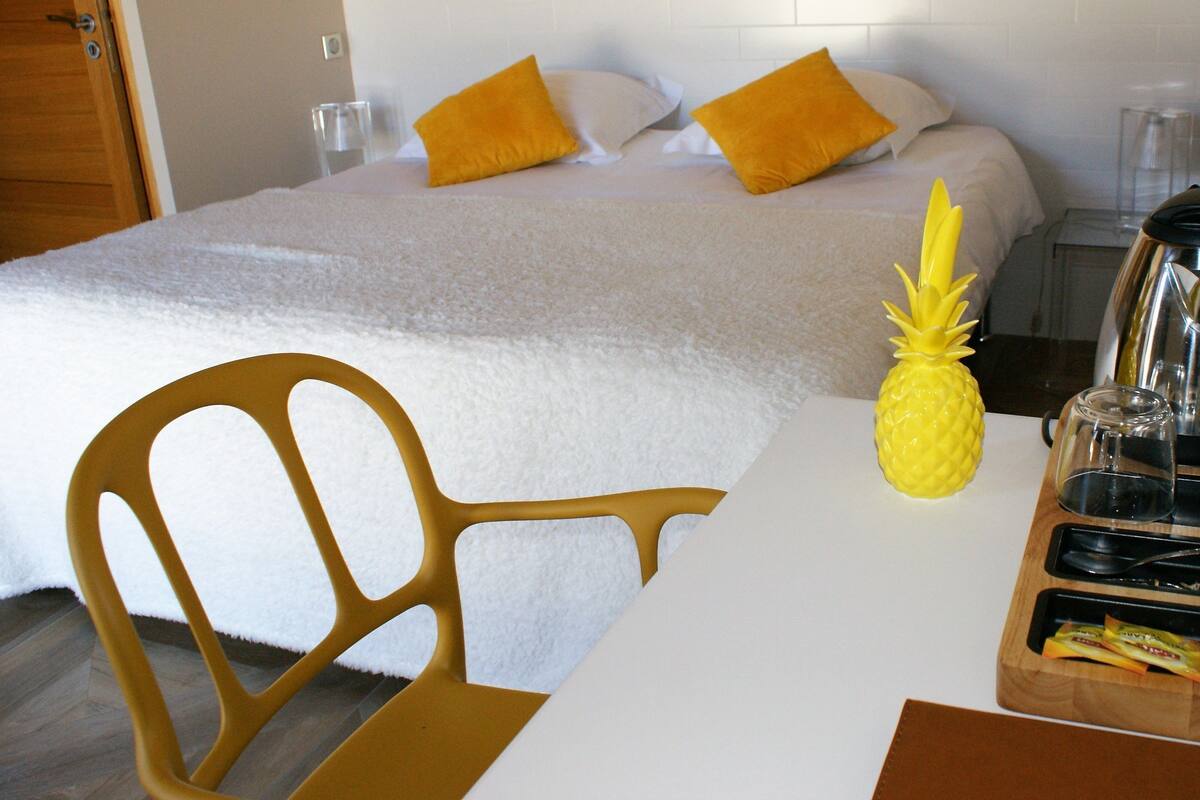 A hotel room with a bed, a wooden chair, a pineapple decoration, a coffee maker, and a tray with snacks.