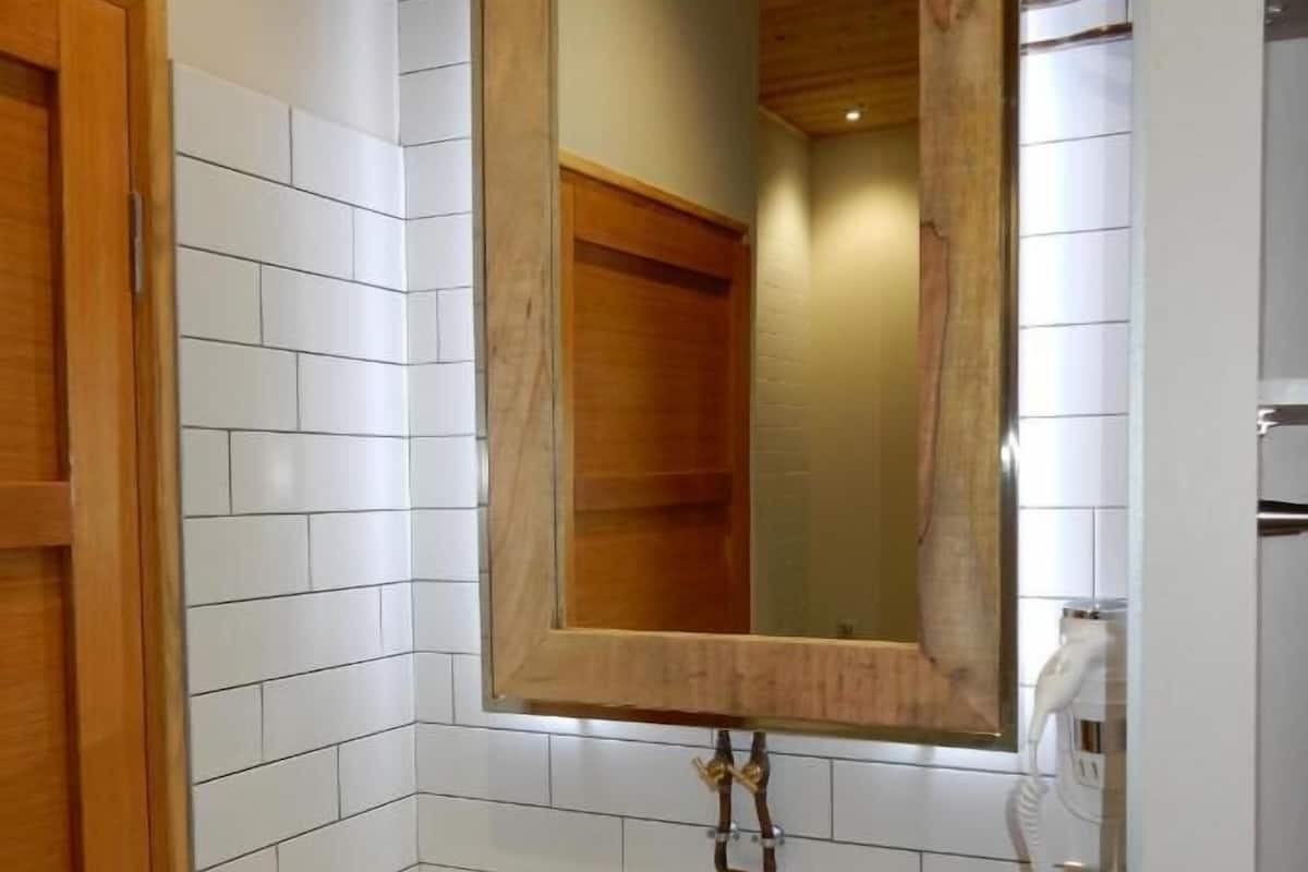 A bathroom with a wooden-framed mirror, white tiled walls, a white sink, and a towel hanging on the wall.