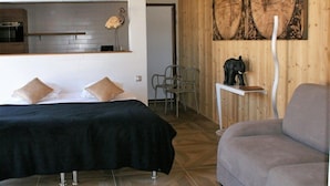 A bedroom with a bed, a sofa, a wooden wall with a map, and a small table with a statue. - What Else Hotel (Saint-Vulbas)