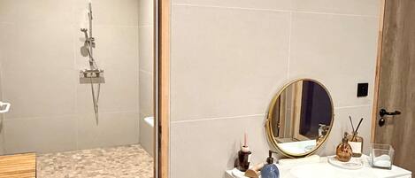 A bathroom with a shower, a vanity with a mirror, a sink, and a small stool.