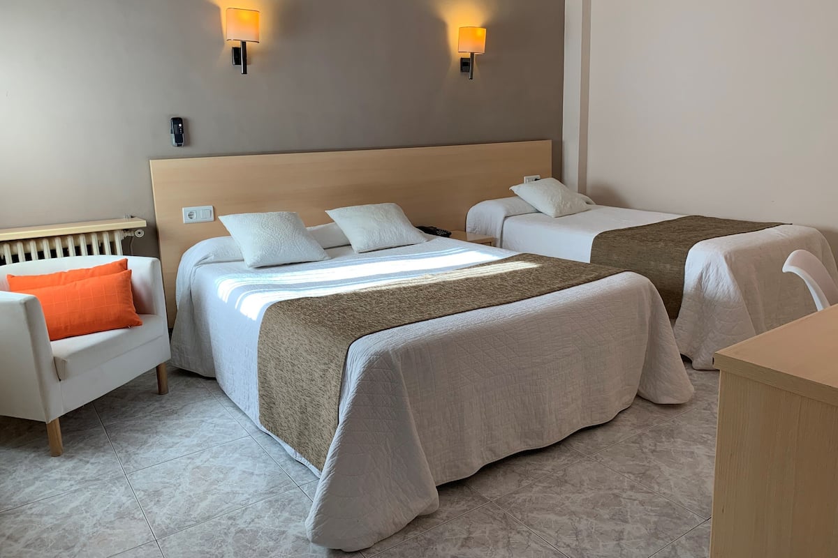 A hotel room with two beds, a sofa, and two wall-mounted lamps.