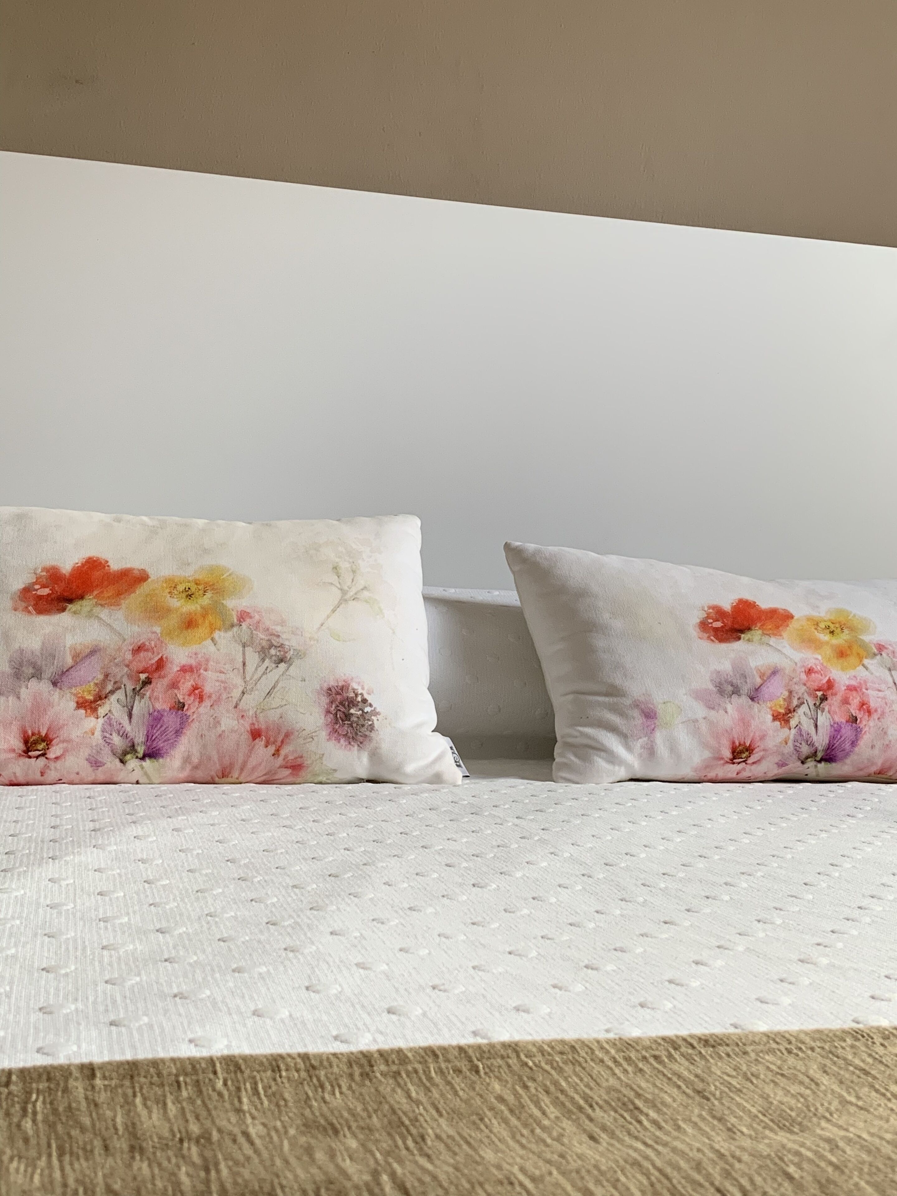 Two pillows with floral designs on a textured white bedspread.