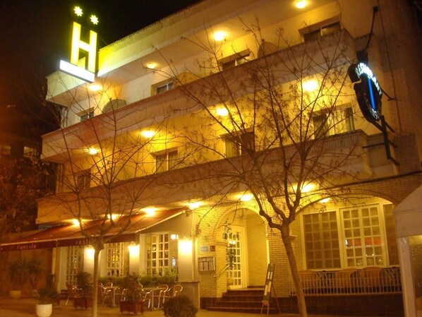 A hotel with a prominent 'H' sign, outdoor seating, and a well-lit entrance. - Hotel Llansola (Sant Carles de la Rapita)