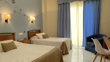 A hotel room with two beds, a desk, a chair, and a large window with blue curtains.