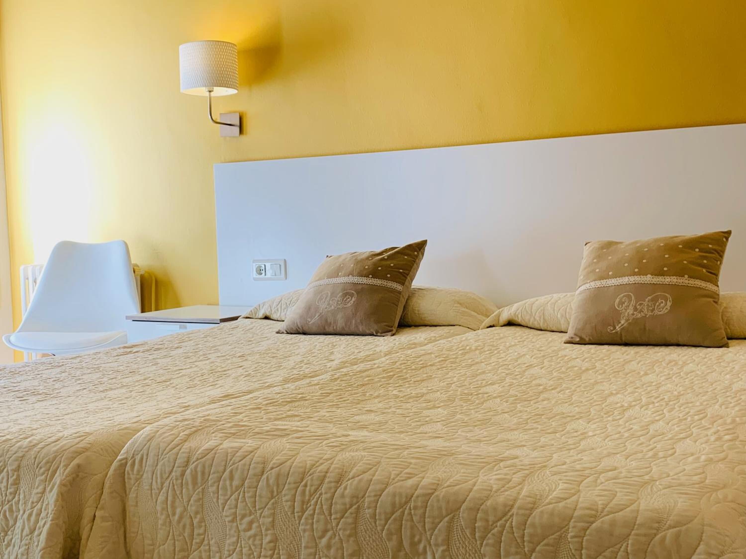 A neatly made bed with a white headboard, two decorative pillows, and a bedside lamp.