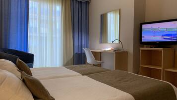 A hotel room with two beds, a desk, a chair, a TV, and a large window with curtains.