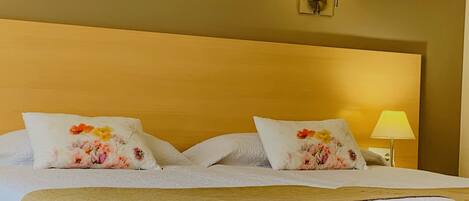 Una cama bien hecha con almohadones florales, una lámpara de noche y una manta acolchada.