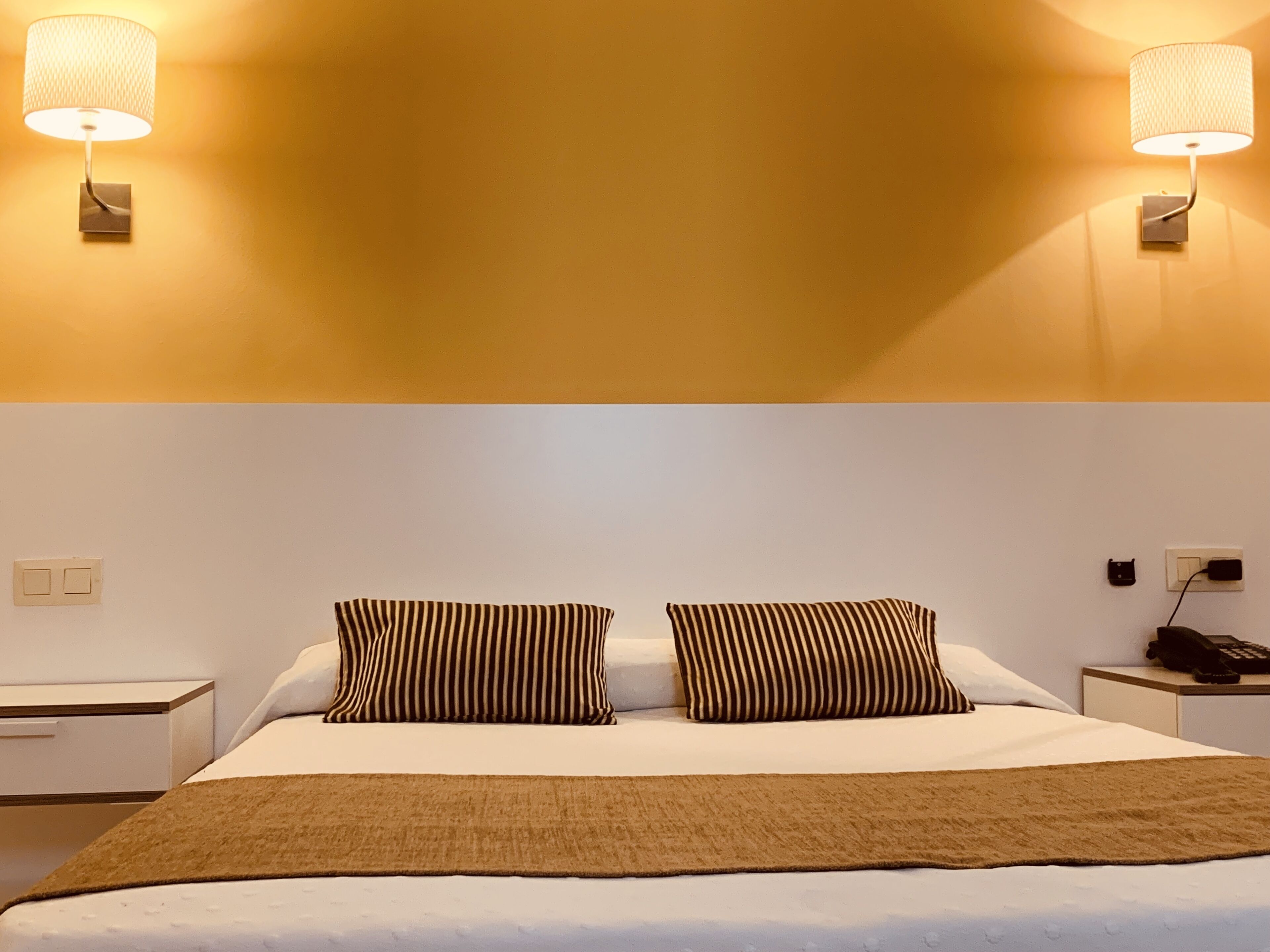 Una habitación de hotel con una cama, dos mesitas de noche, una lámpara y un teléfono.