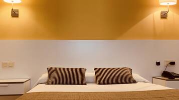 Una habitación de hotel con una cama, dos mesitas de noche, una lámpara y un teléfono.