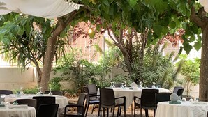 Un espace extérieur aménagé pour les repas, avec des tables et des chaises, entouré de verdure et d’arbres.