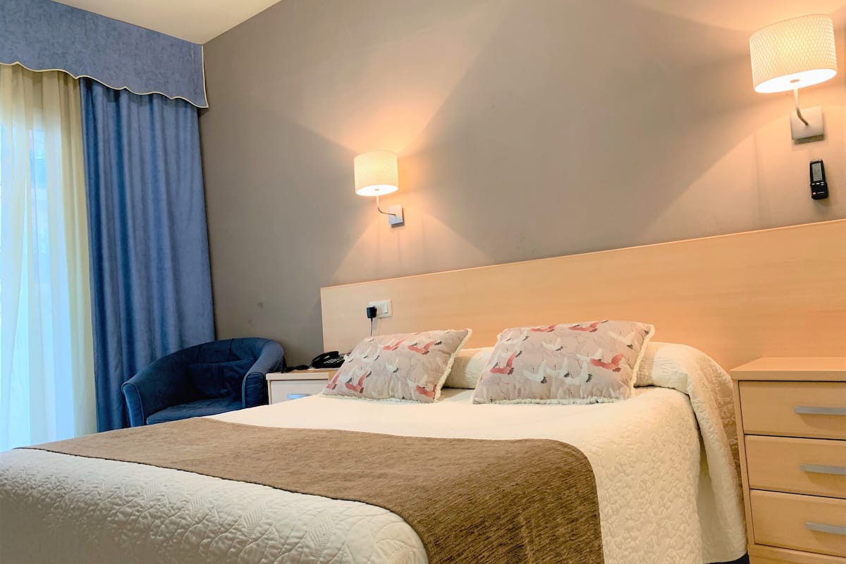 A hotel room with a large bed, a bedside table with a lamp, a chair, and a nightstand.