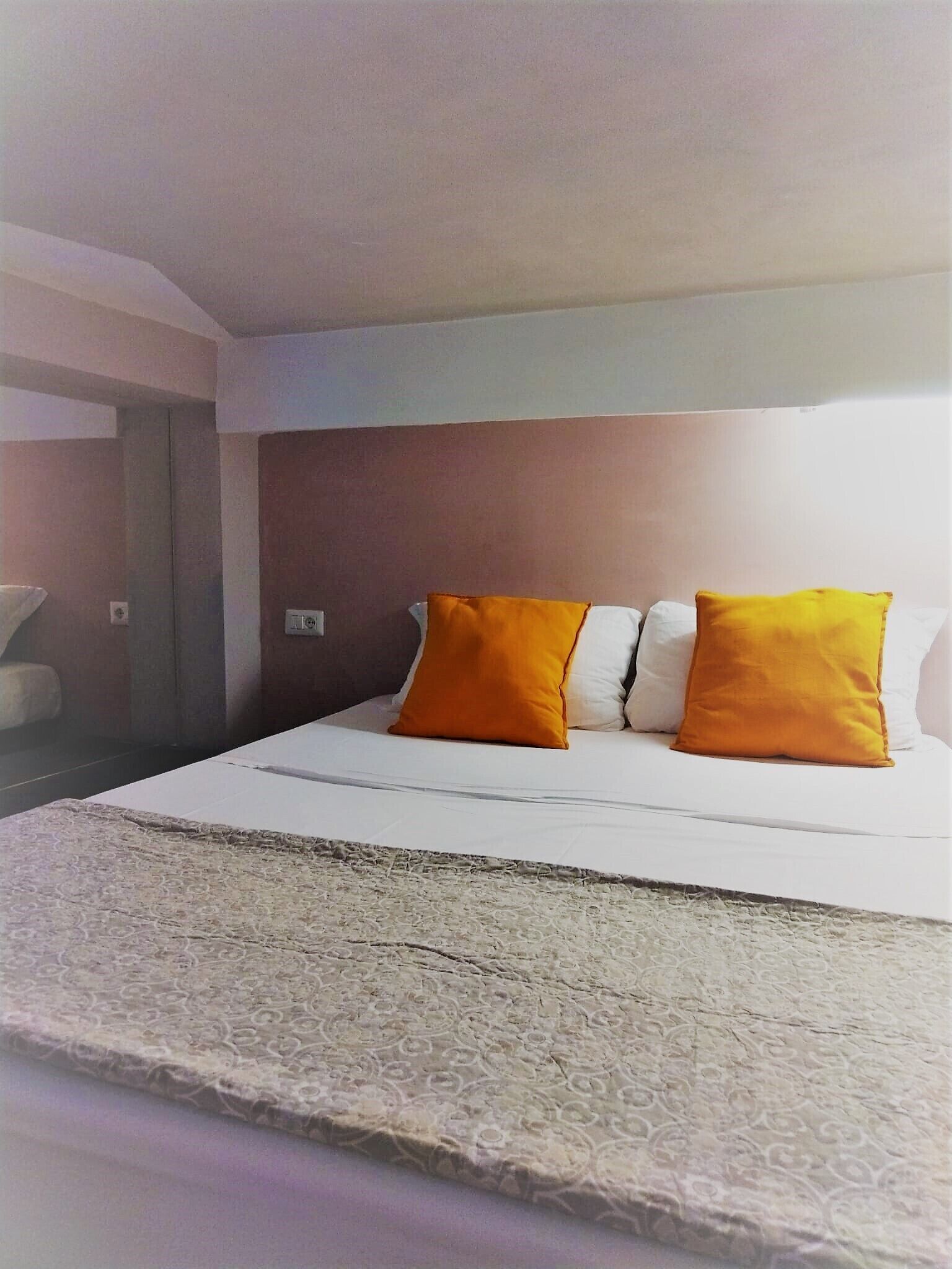 A hotel room with a bed, two pillows, a bedside table, and a lamp.