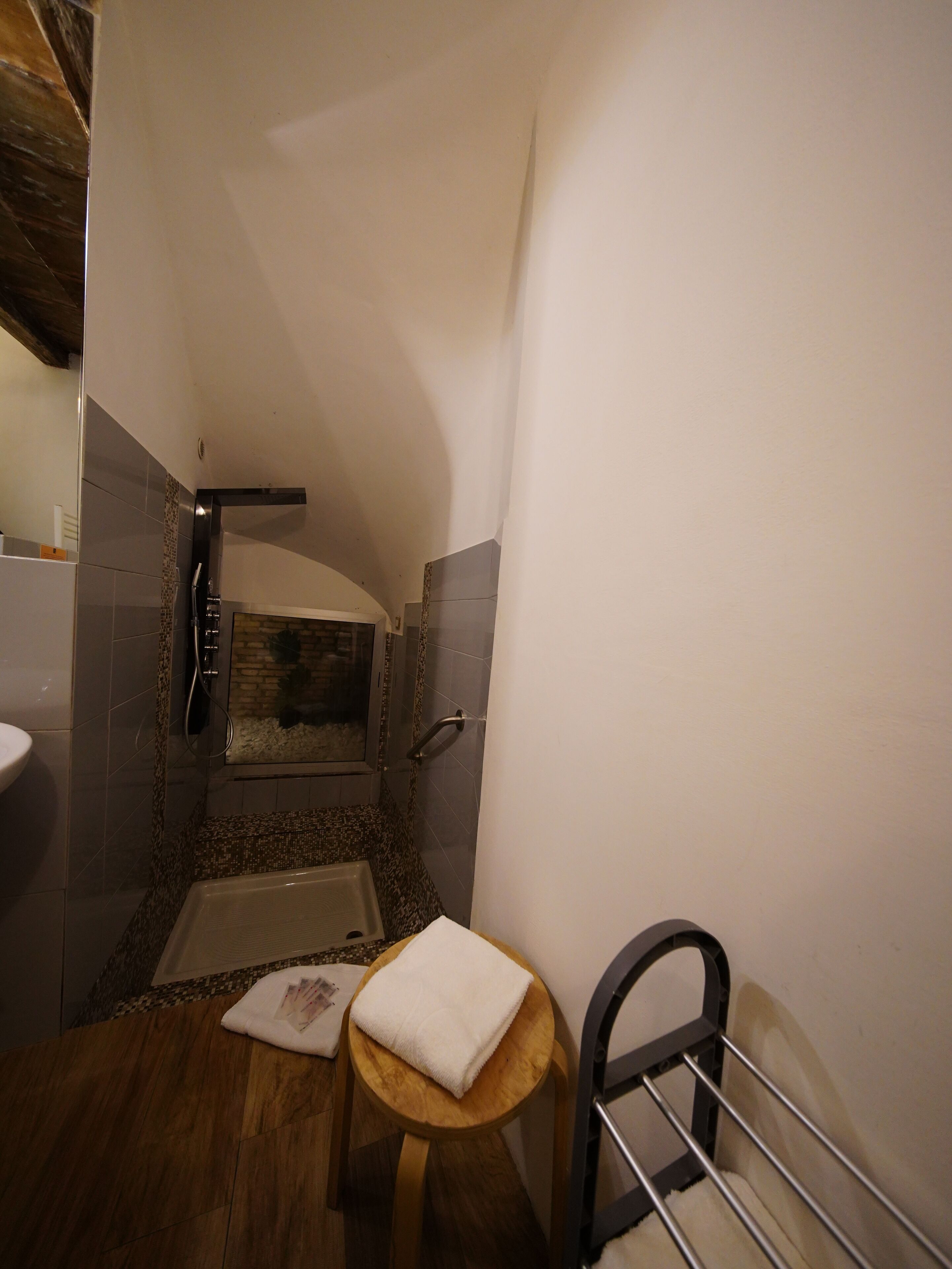 Un baño con ducha, lavamanos y un taburete de madera con una toalla.