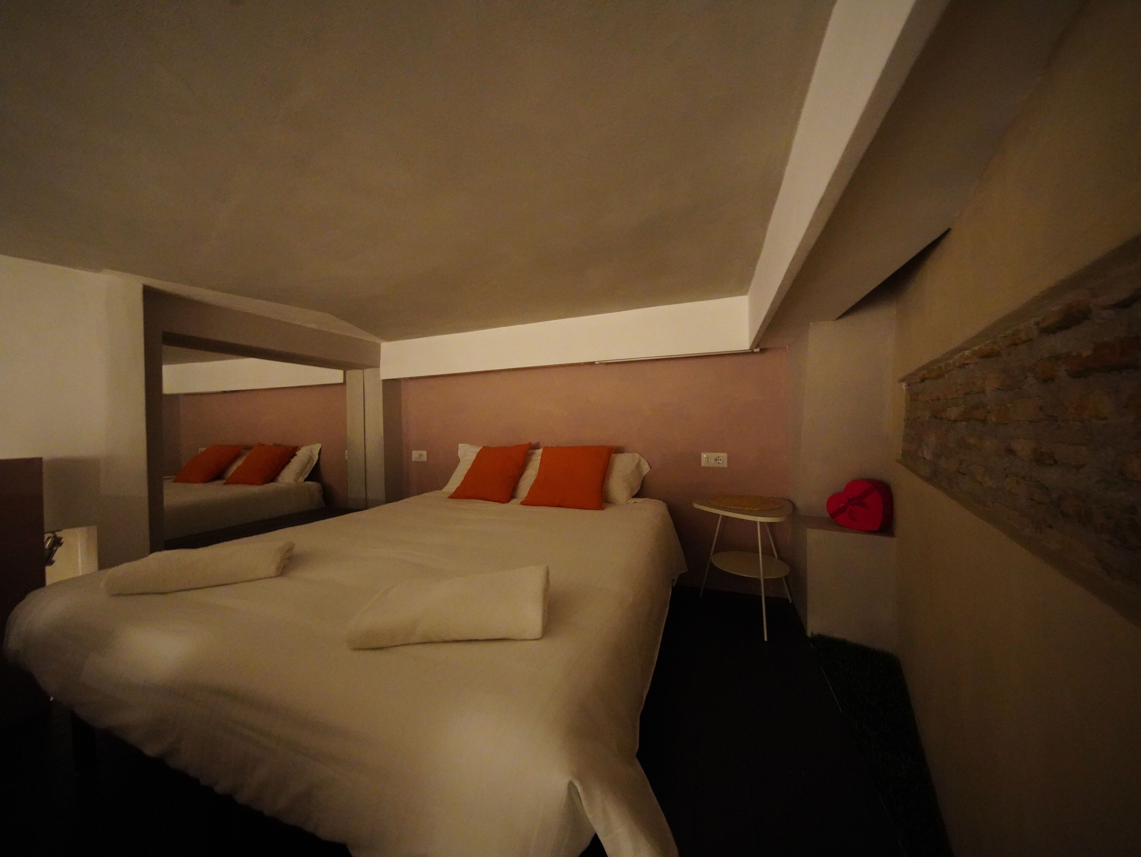 A hotel room with a large bed, a smaller bed in the corner, a small table, and a red hat on the wall.
