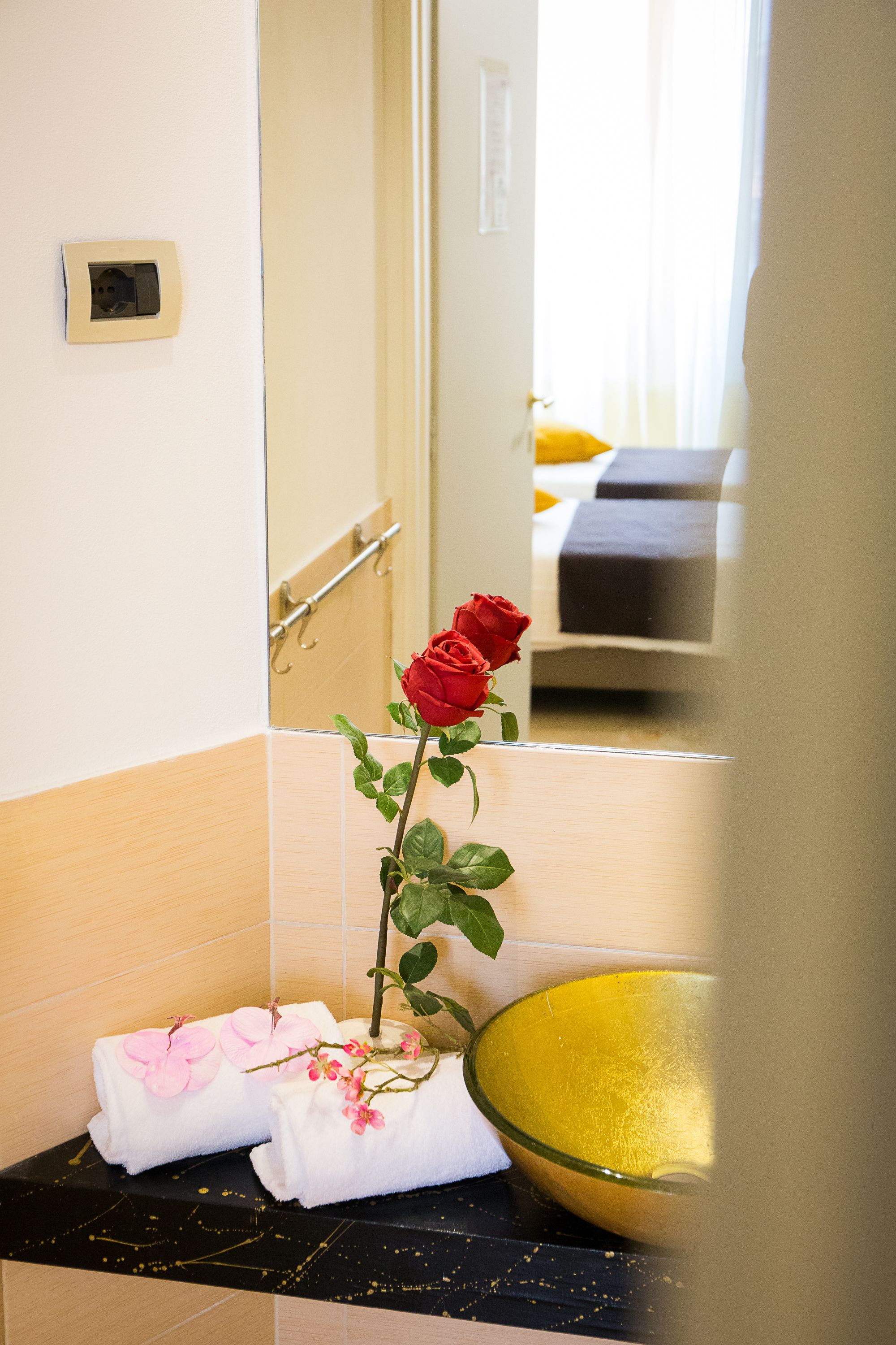 Een badkamer met een spiegel, een wastafel met een gele kom en handdoeken met roze bloemen.