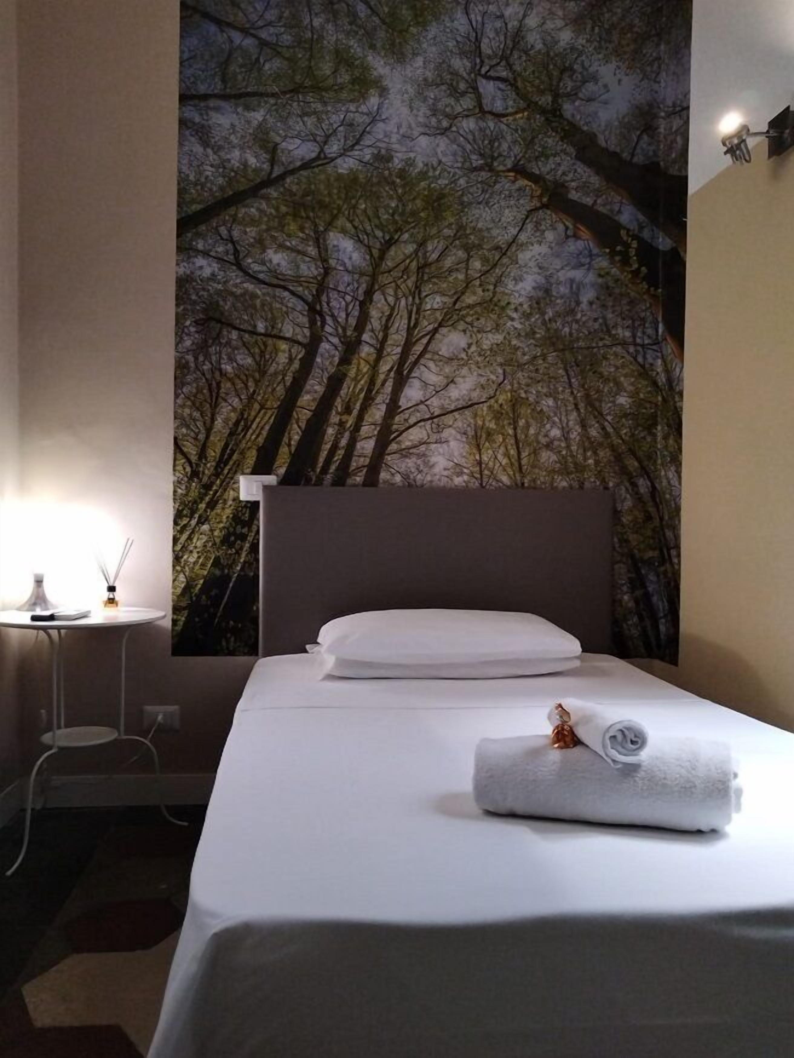Une chambre d’hôtel avec un lit, une table de chevet, une lampe et une fresque murale représentant des arbres.