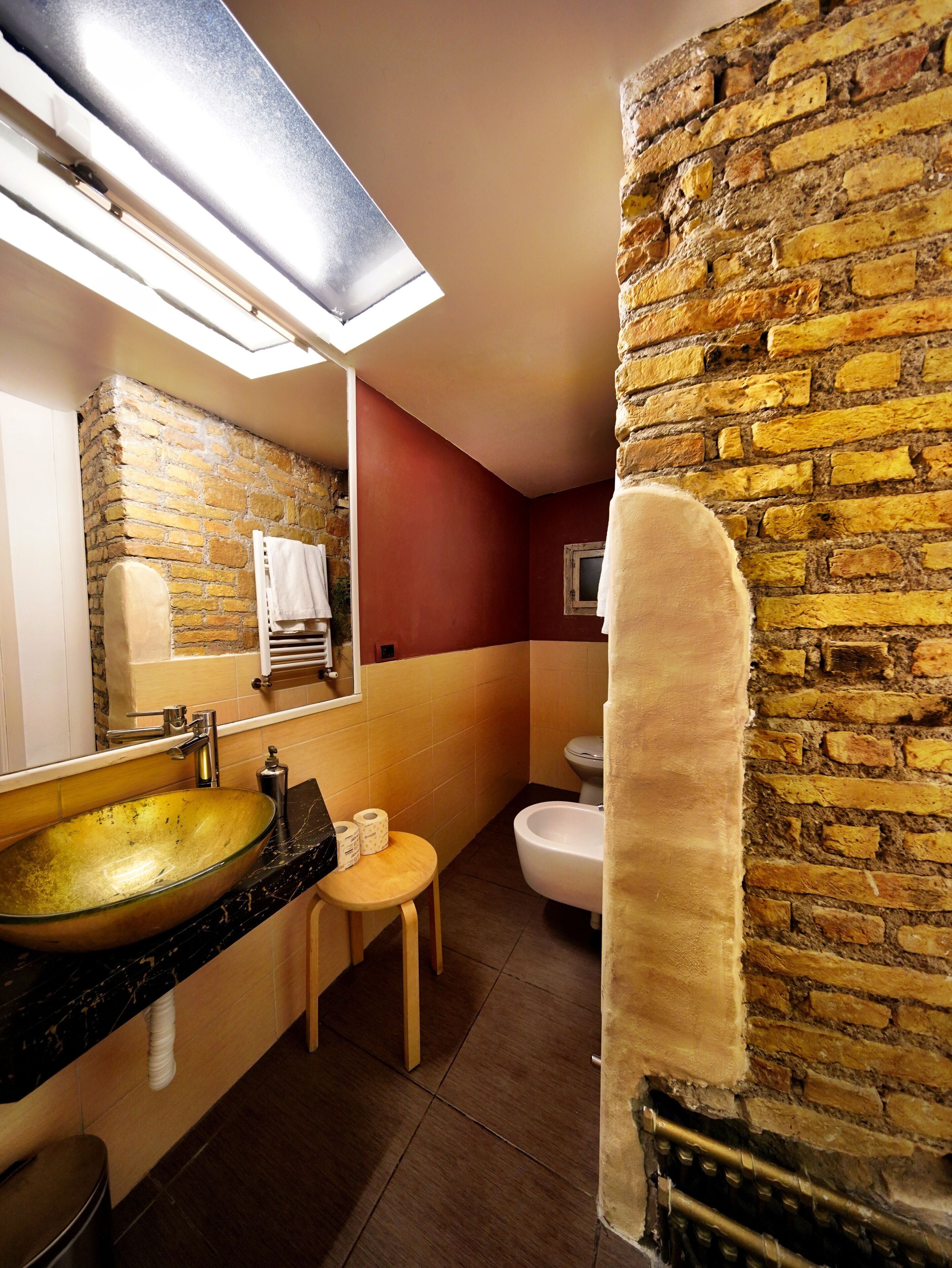 Une salle de bain avec un grand lavabo en verre, un miroir, un porte-serviettes, des toilettes et un petit tabouret en bois.