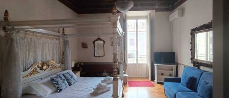 Un dormitorio con cama con dosel, televisor y sofá azul.