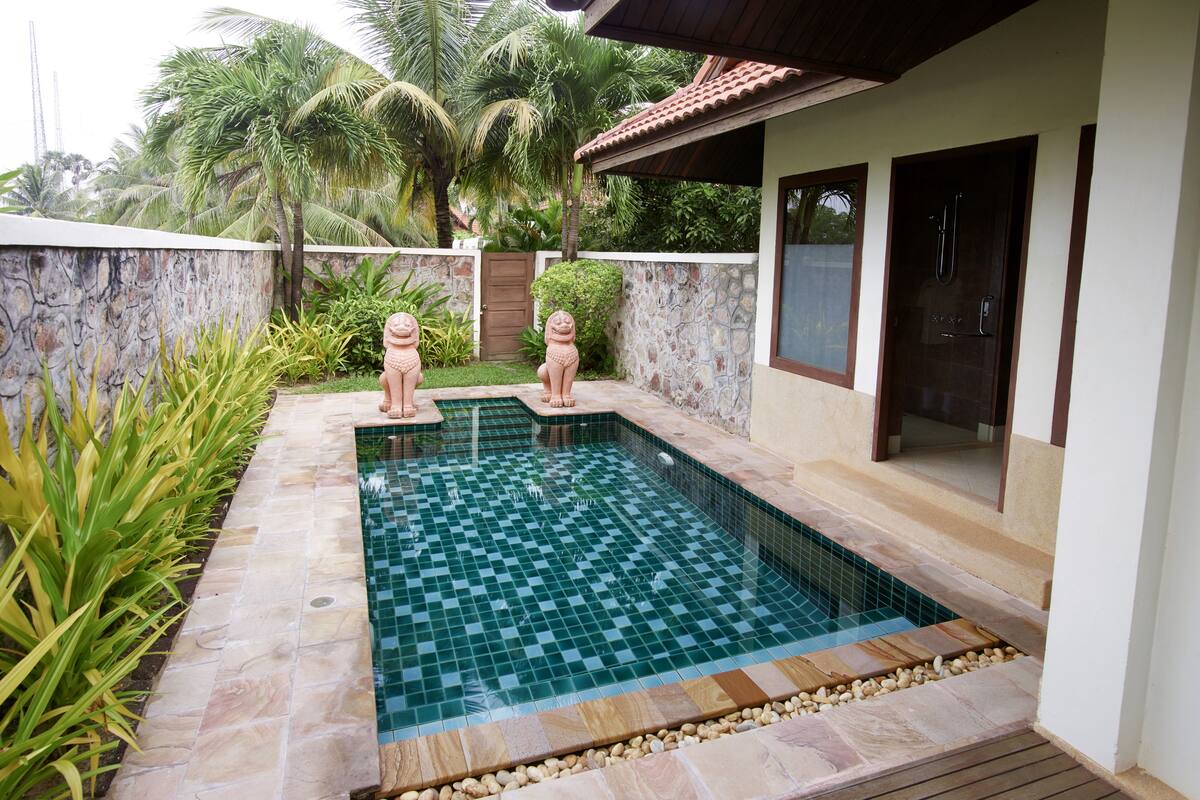A rectangular swimming pool with checkered tiles, surrounded by a stone wall and wooden deck.