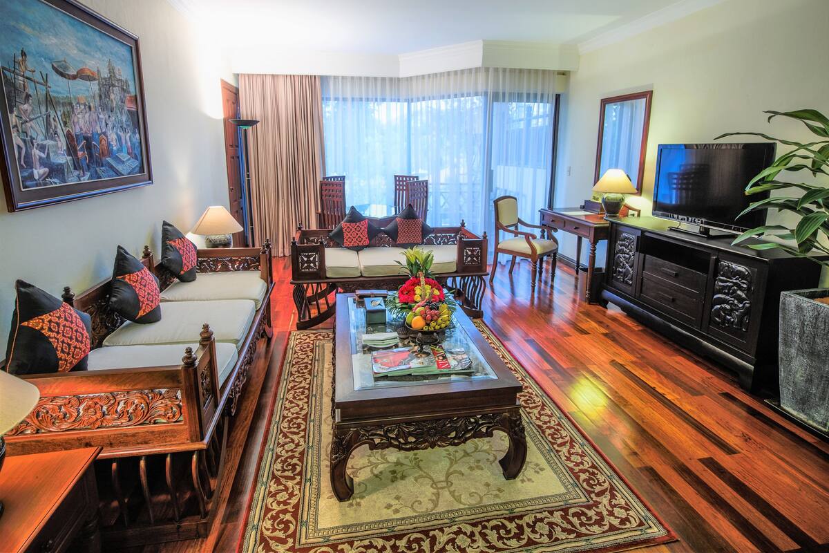 A traditional living room with a sofa set, a coffee table with fruit, a television, and a painting on the wall.