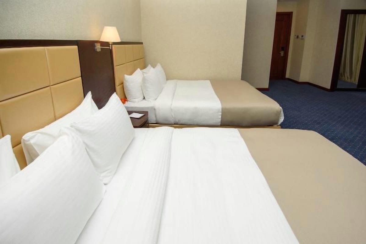 A hotel room with two beds, a nightstand, and a lamp.