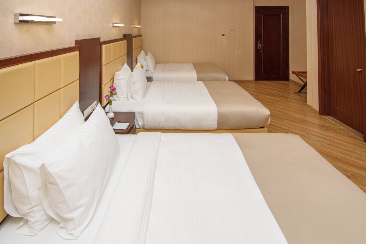A hotel room with three beds, a wooden headboard, a nightstand with a vase of flowers, and a wooden door.