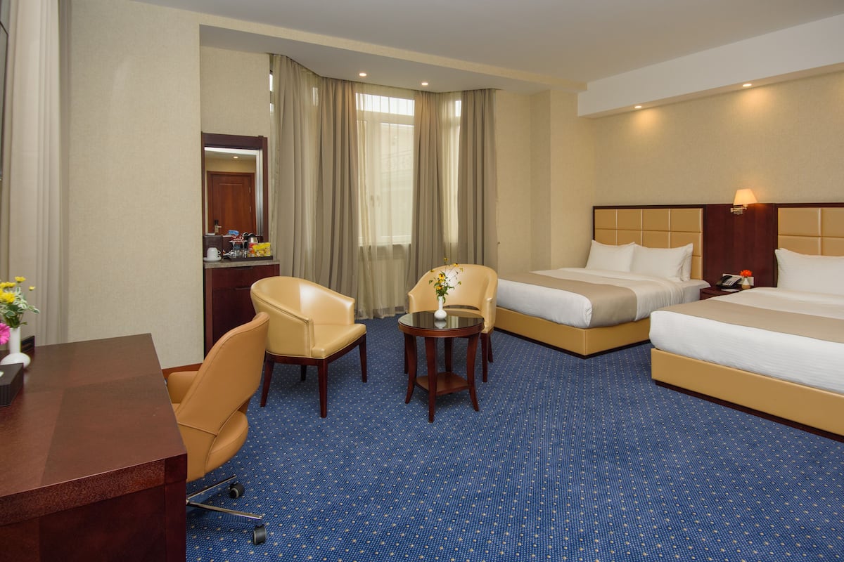 A hotel room with a large bed, a smaller bed, a desk, a chair, and a small table with a vase.