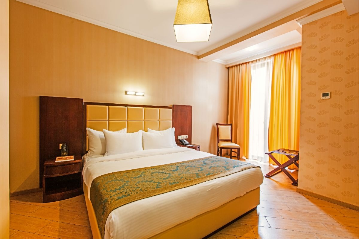 A hotel room with a large bed, a nightstand, a chair, and a window with curtains.