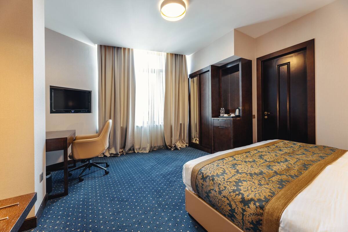 A hotel room with a bed, a desk, a chair, a TV, and a wardrobe.