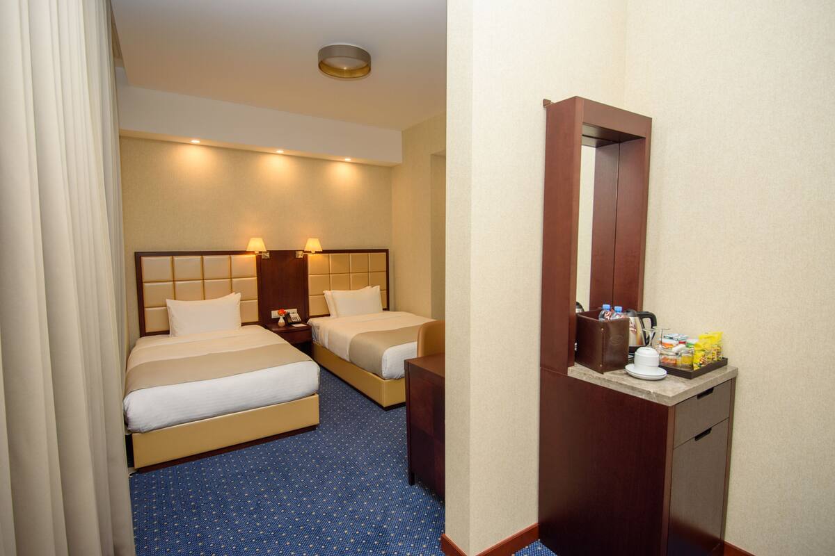 A hotel room with two beds, a small desk, a mirror, and a minibar.