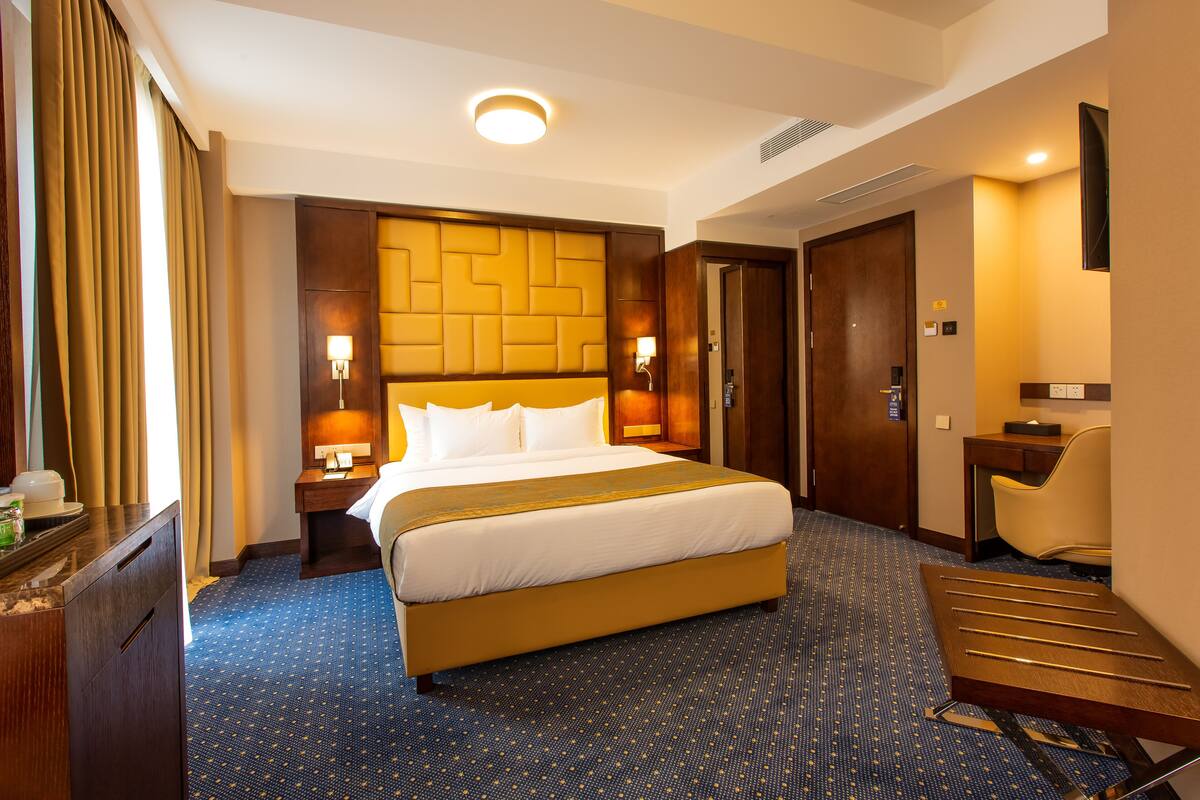 A hotel room with a large bed, a desk, a chair, a wardrobe, and a bathroom door.