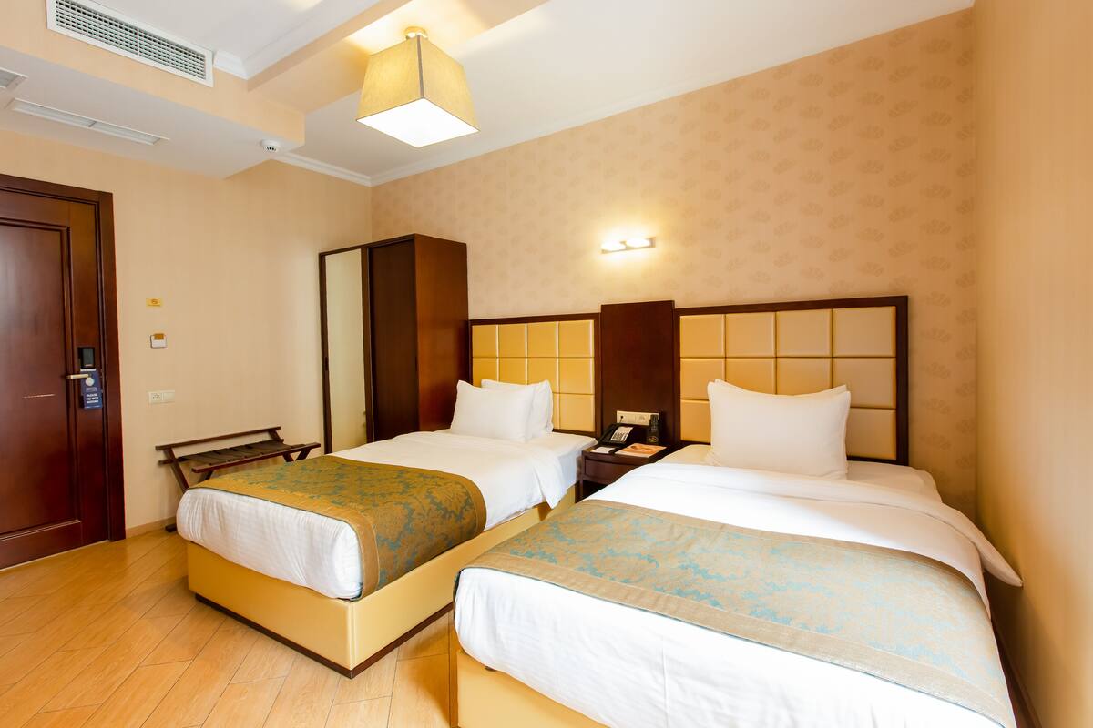 A hotel room with two beds, a wooden bench, a wardrobe, and a nightstand with a phone.